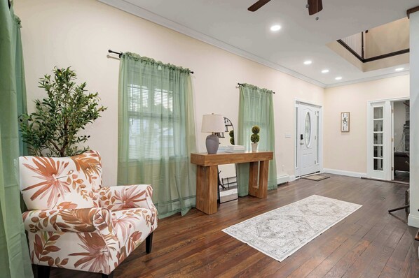 A living room with a wooden floor, a floral sofa, a wooden coffee table, and a green plant.