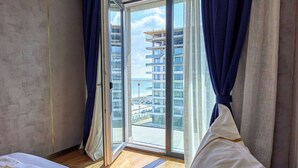 A hotel room with a bed, a view of a building across the street, and a sliding glass door. - Signature Mamaia Nord (Mamaia-Sat)