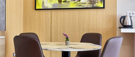 A dining area with a round table, four chairs, and a painting on the wall.