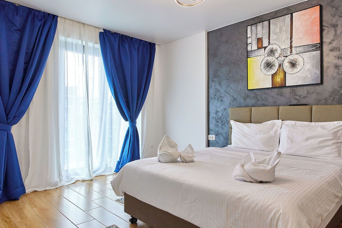 A hotel room with a bed, white bedding, a headboard, and a painting on the wall.