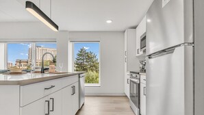 Cozinha moderna com uma ilha grande, armários brancos e vista para um edifício pela janela.
