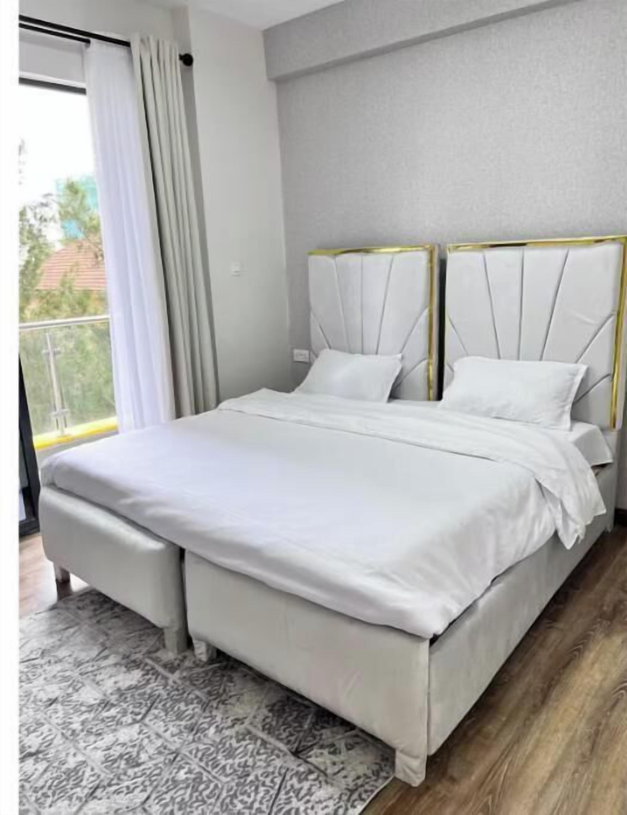A modern bedroom with a large bed, a small bedside table, and a view of the outdoors.