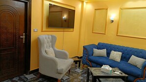 A room with a wooden door, a grey armchair, a blue sofa, and a small table with a remote control. - THE MESSAHA ROYALE (Giza Governorate)