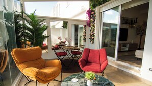 A modern living room with a glass door leading to a balcony, furnished with a red chair, a yellow armchair, and a marble coffee table.