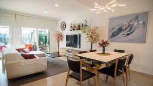 A modern living room with a white sofa, a dining table with chairs, a fireplace, and a large window.