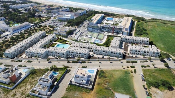 A coastal resort with multiple buildings, a beach, and a pool area.