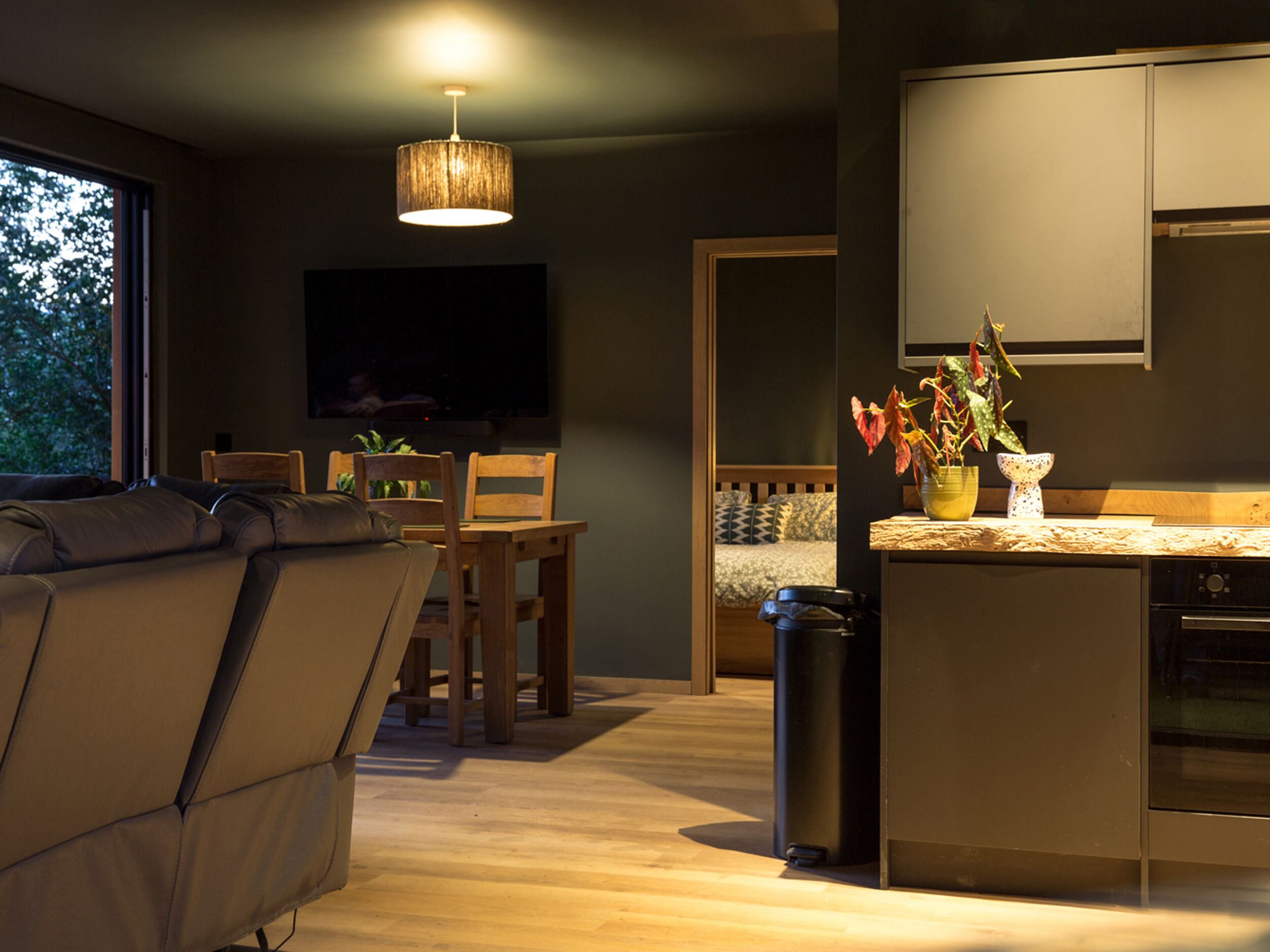 A modern kitchen with a dining area, wooden furniture, and a large window.
