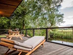 A wooden deck with a lounge chair and a table, overlooking a body of water and trees. - The Red House (Chester)