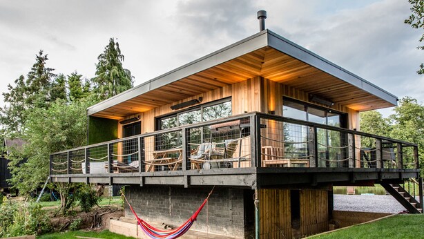Una casa moderna con terraza de madera, una hamaca y vistas al verde circundante.
