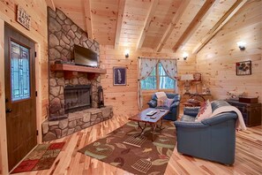 Interior acogedor de una cabaña con chimenea de piedra, paredes de madera, un sofá azul y un tapete estampado.