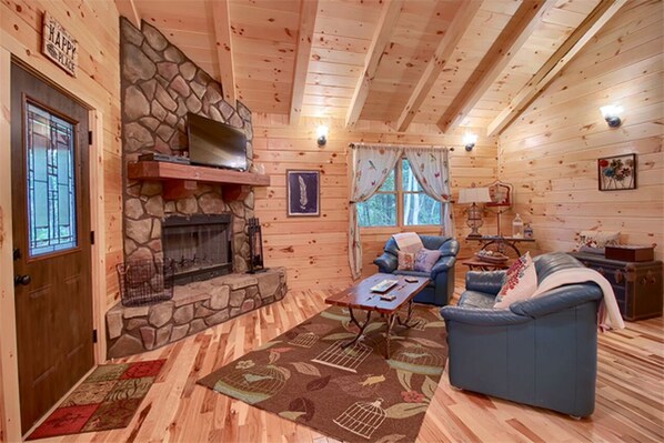 Interior acogedor de una cabaña con chimenea de piedra, paredes de madera, un sofá azul y un tapete estampado.