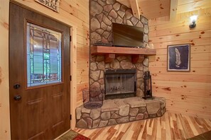 A wooden interior with a stone fireplace, a door with a window, and a wall-mounted light fixture.