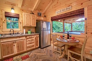 Ein Holzblockhaus-Interieur mit Küche, Essbereich und einem Fenster mit Blick auf Grünflächen.