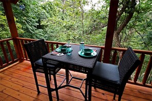 Terraza de madera con mesa y sillas, rodeada de abundante vegetación.