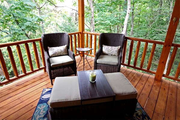 A wooden deck with wicker chairs and a table, surrounded by trees.