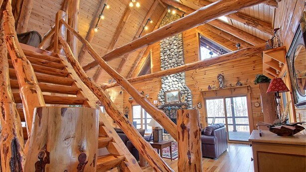 Ein Holzblockhaus-Interieur mit Kamin aus Stein, einer Holztreppe und einem gemütlichen Wohnbereich.