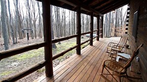 Eine Holzterrasse mit Geländer, Holzstühlen und Blick auf einen Wald.