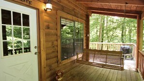Eine Holzhütte mit Veranda, einer weißen Tür mit freundlicher Begrüßung und einer Bank.