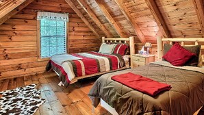 Ein gemütliches Schlafzimmer im Dachgeschoss mit zwei Betten, Holzbalken, einem Fenster und einem Kuhfellteppich.