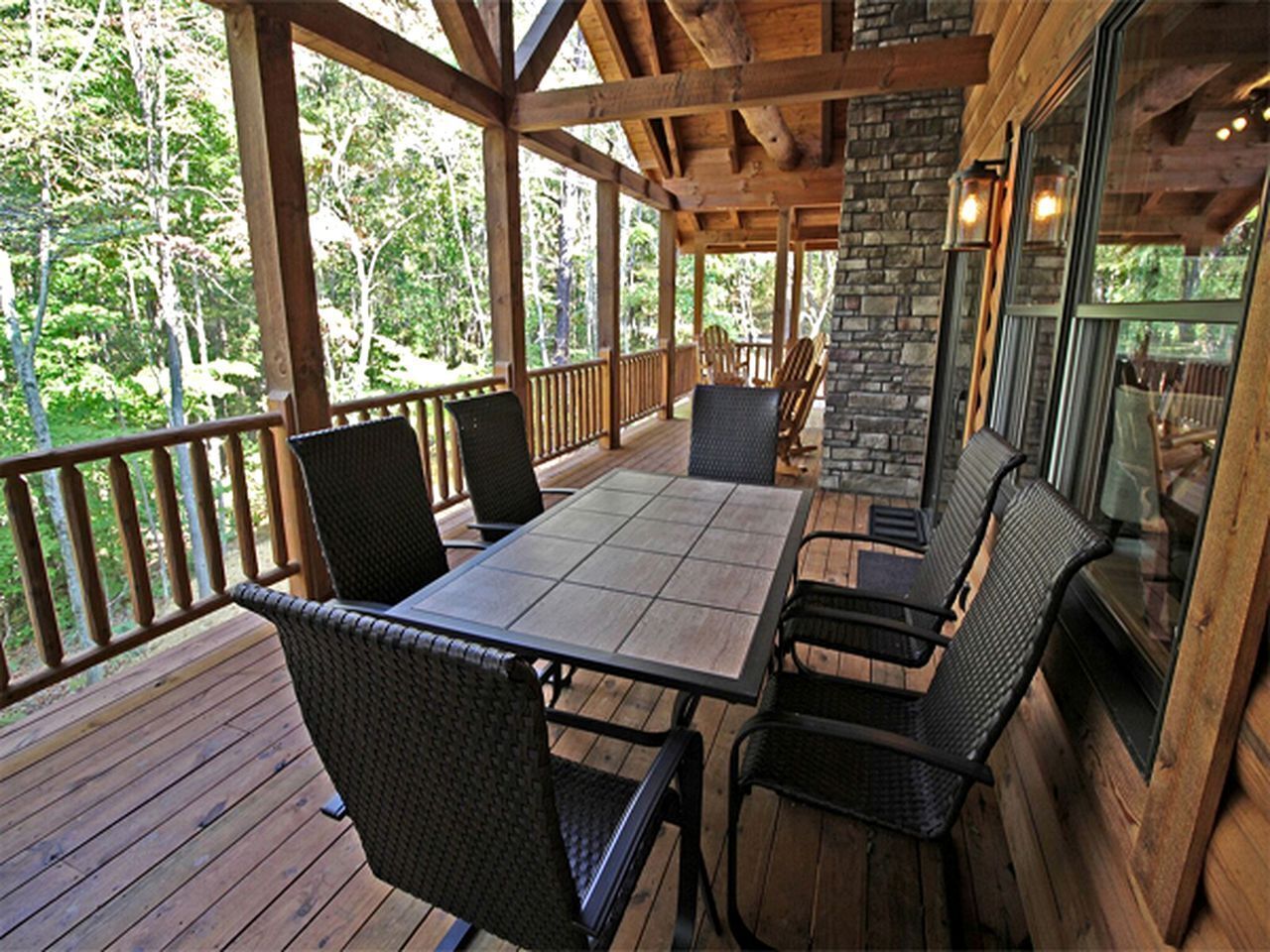 Une terrasse extérieure couverte, dotée d’une table et de chaises, et entourée de rampes en bois et d’un mur en pierre.