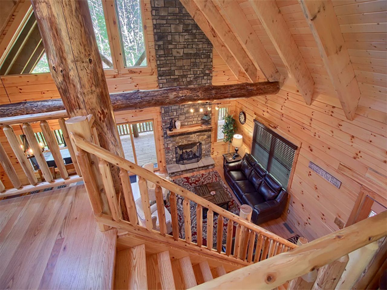 Ein Holzblockhaus-Interieur mit Kamin aus Stein, einer Ledersofa und einer Holztreppe.