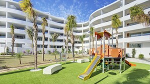 A playground with a slide and climbing structures, surrounded by palm trees and a white building with multiple balconies. - Ref. 585392 (Motril)