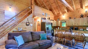 A wooden cabin interior with a sofa, dining table, chairs, and a kitchen area. - Luxury Lodge for Big Groups in Hocking Hills, Ohio (Logan)
