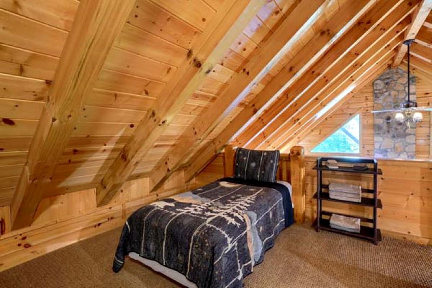 A cozy attic bedroom with a bed, a stone wall, and a wooden ceiling.