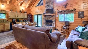A cozy cabin interior with a stone fireplace, wooden walls, and a dining area. - Luxury Lodge for Big Groups in Hocking Hills, Ohio (Logan)