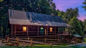 A log cabin with a porch, surrounded by trees and a body of water. - Luxury Lodge for Big Groups in Hocking Hills, Ohio (Logan)