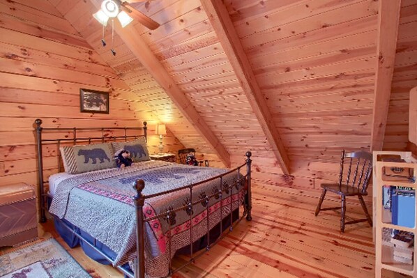 A cozy attic bedroom with a sloped ceiling, a wooden bed, a chair, and a small table.