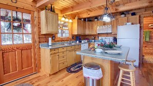 A wooden cabin kitchen with a central island, wooden cabinets, a refrigerator, and a window with a view of trees.