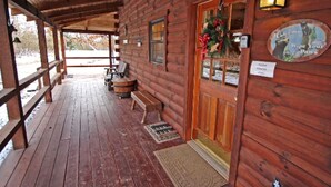 A wooden cabin with a porch, a door with a wreath, and a sign that says "Wipe Your Paws".