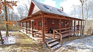 A wooden cabin with a porch, steps leading to the entrance, and a clear sky.