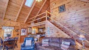A cozy cabin interior with a dining area, a sofa, and a staircase leading to an upper level.