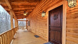 Une cabane en bois dotée d’un porche couvert, d’une porte en bois sombre et de deux lanternes fixées au mur.