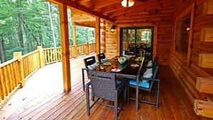 Eine Holzhütte mit Essbereich, inklusive Tisch und Stühlen, Deckenventilator und Blick auf den umliegenden Wald.