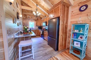 A wooden cabin kitchen with a refrigerator, wooden cabinets, a white bench, and a blue shelf.