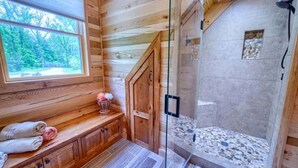 A wooden cabin interior with a glass-enclosed shower, a window with a view of trees, and a wooden bench with towels. - Wonderful Ohio Vacation Rental for Nature Getaways near Hocking Hills Park (Logan)