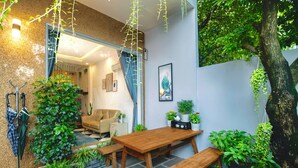 A cozy indoor garden with a wooden table and benches, surrounded by lush plants and a hanging plant. - Healing home I 3 minutes ride to the Beach I Garden & BBQ (Đà Nẵng)