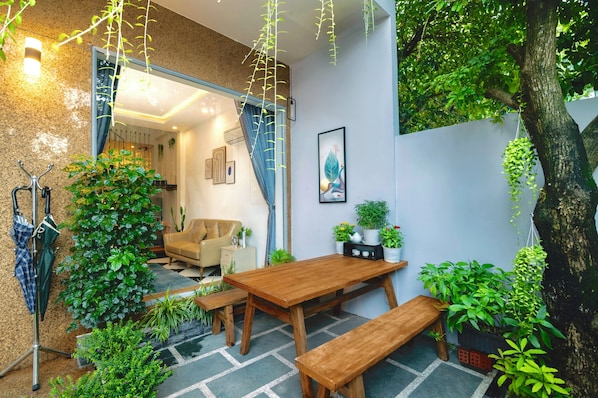 Un jardín interior acogedor con una mesa y bancos de madera, rodeado de plantas exuberantes y una planta colgante.