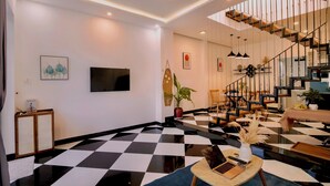 A modern living room with a black and white checkered floor, a staircase, and a flat-screen TV mounted on the wall. - Healing home I 3 minutes ride to the Beach I Garden & BBQ (Đà Nẵng)