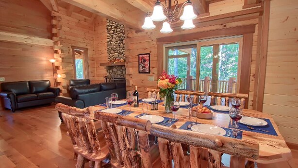 L’intérieur d’un chalet en bois présente une table à manger dressée pour quatre personnes, entourée de chaises en bois rustiques.