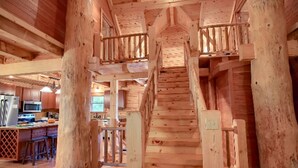 Un intérieur en bois avec un escalier central, des poutres apparentes et un espace cuisine équipé d’appareils modernes.