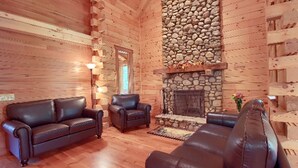 L’intérieur d’une cabane en rondins, avec une cheminée en pierre, des canapés en cuir et un plancher en bois.