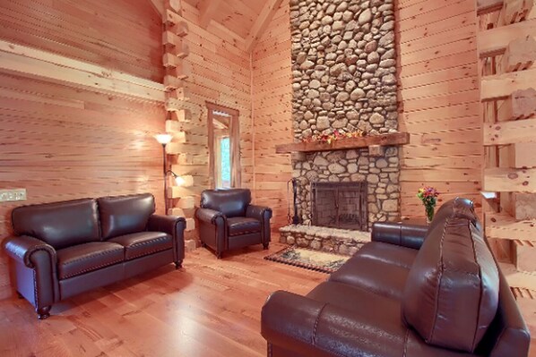 A log cabin interior with a stone fireplace, leather sofas, and a wooden floor. - Stately Log Cabin with a Hot Tub Perfect for a Weekend Getaway near Columbus, Ohio (Logan)