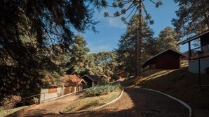 A paved pathway leading to a building with a red roof, surrounded by trees and a clear sky. - Pousada dos Quatis (Campos do Jordão)