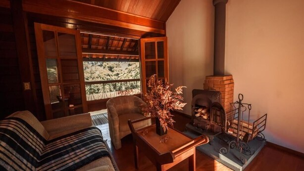 A cozy living room with a fireplace, a sofa, and a dining table. - Pousada dos Quatis (Campos do Jordão)