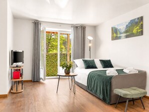 A modern hotel room with a bed, a TV, a small table with a plant, and a painting on the wall.
