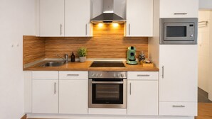 A modern kitchen with white cabinets, a stainless steel oven, a microwave, and a wooden backsplash.